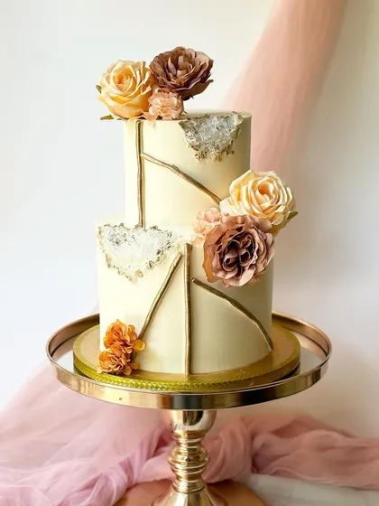A chic and modern two-tier cake with clean lines and a unique geode-inspired fault line design in gold. The cake is finished with elegant brown and peach-toned sugar flowers for a contemporary look.