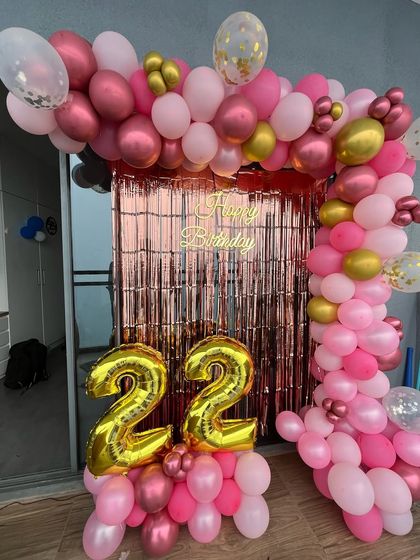 A pretty pink and rose gold theme for a 22nd birthday. The balloon arch frames a rose gold shimmer curtain, with large number '22' foil balloons in the front.