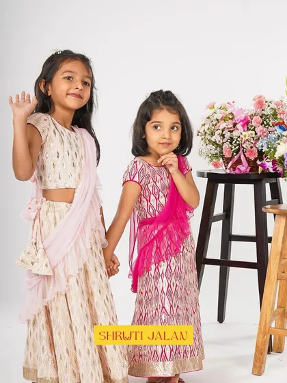 Two sisters, one in a cream printed lehenga and the other in a pink version. They show how you can coordinate in different colors of the same style.
