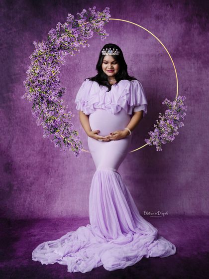 A vision in lavender. This mom-to-be is framed by a floral wreath, wearing a crown and a gorgeous off-shoulder gown for a truly royal portrait.