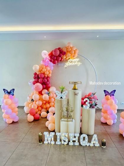 A lovely butterfly theme for a third birthday. This setup uses a simple ring frame with a peach and pink balloon garland, butterfly accents, and light-up letters for the name 'Mishqa'.
