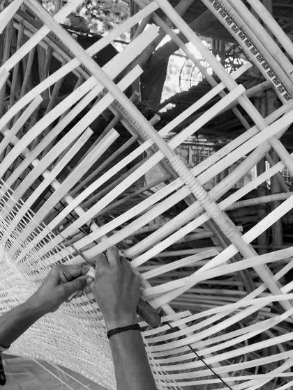 This is where design comes to life. An artisan's hands meticulously weave cane onto the framework for the Biergarten light fixture. This behind the scenes view shows the dedication and skill involved in our collaborative craft process.
