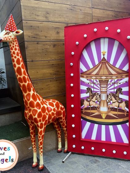 A whimsical carnival prop featuring a giraffe in a party hat next to a carousel-themed photo frame.