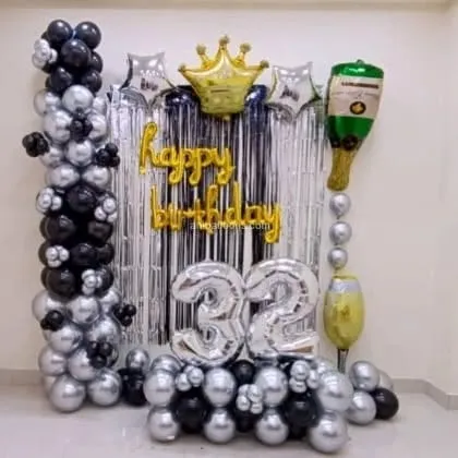 A simple home birthday decoration with a silver shimmer curtain, black and silver balloon columns, and a '32' foil balloon.
