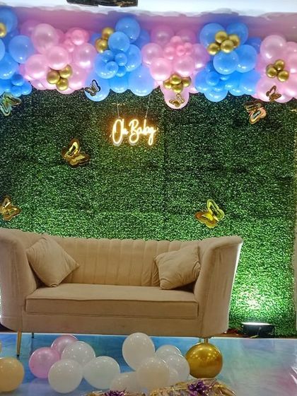 A beautiful baby shower stage with a grass wall backdrop, a pink and blue balloon arch, and a comfortable sofa for the mom to be.