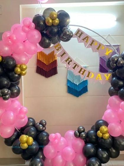 A trendy pink and black balloon ring decoration. This setup is perfect for a stylish at-home party, with a "Happy Birthday" banner and boho-style wall hangings.