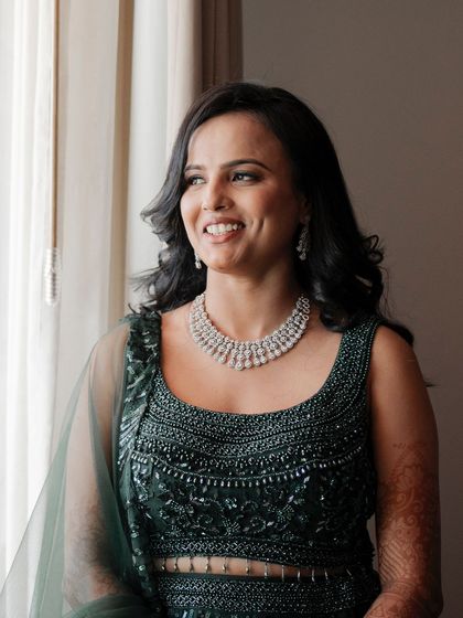 A beautiful portrait of the bride looking out a window. The soft, natural light highlights her features and the delicate details of her green lehenga.