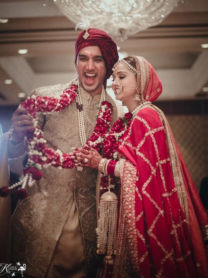 A fun, celebratory moment during the jaimala ceremony, with the groom holding up the garland in victory.