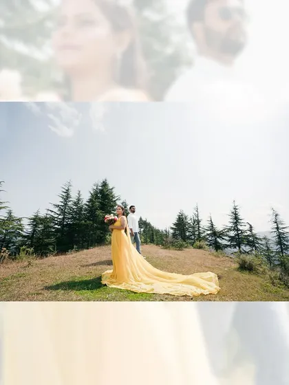 A wide shot of a woman in a stunning yellow trailing gown, standing on a hilltop with her partner, set against the vast mountain landscape.
