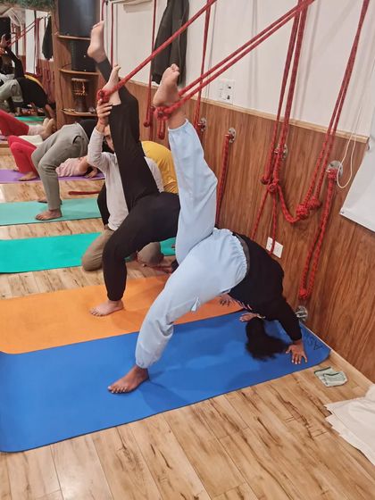 Students use the wall ropes to work on one-legged wheel pose variations. This builds strength and flexibility in a supported and controlled manner.
