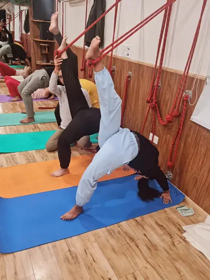 Students use the wall ropes to work on one-legged wheel pose variations. This builds strength and flexibility in a supported and controlled manner.