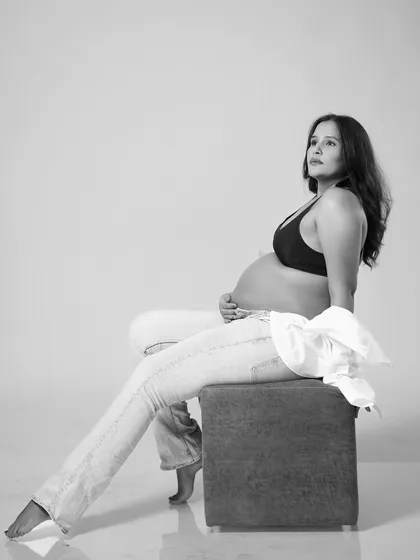 A striking black and white portrait of the mother-to-be. This modern, seated pose in jeans and a bra top creates a confident and artistic image celebrating the female form during pregnancy.
