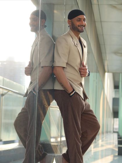 Harbhajan Singh leaning against a glass wall, reflecting his cool demeanor in our custom beige blazer.