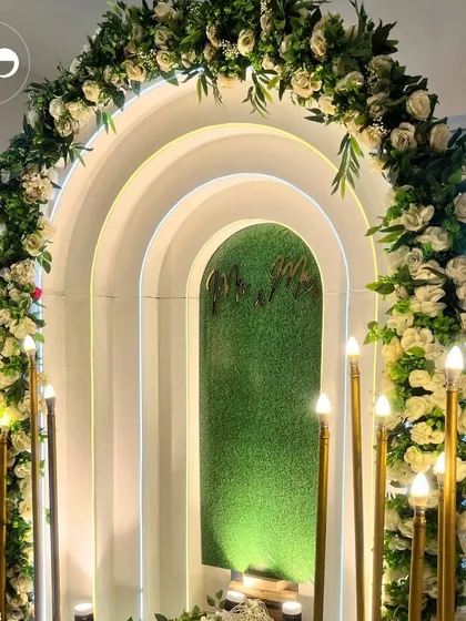 A full view of the elegant white and green floral arch, perfect for an indoor engagement or anniversary celebration. The integrated LED lighting and candle-style floor lamps create a truly magical ambiance.
