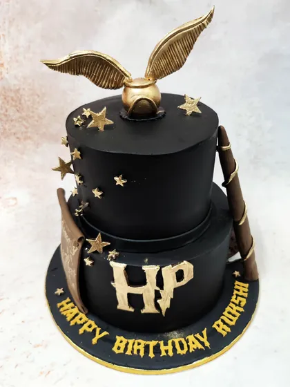 We bring a touch of magic to your celebration with this two-tier Harry Potter cake. The design features iconic elements like the golden snitch, a wizard's wand, and the HP logo in a gothic font, all set against a dramatic black backdrop to capture the mystique of the wizarding world.