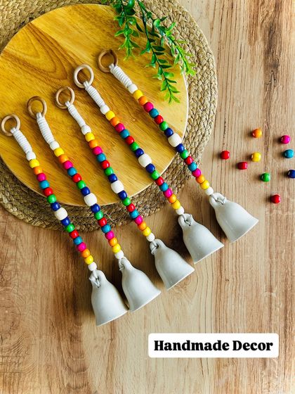 Our 'Rainbow Bells' are one of our cutest creations. This flat lay shows the mini ivory ceramic bells with vibrant wooden beads, a perfect handmade decor piece to brighten up your home.