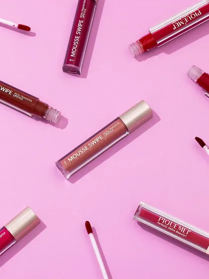 A dynamic flatlay of liquid lipsticks and their applicators on a vibrant pink background. This kind of scattered yet organized composition is great for showing off a range of shades in a playful way.