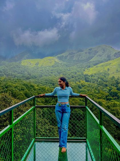 A trekker standing on the glass bridge at 900 Kandi in Wayanad, with a stunning view of the green valley below.
