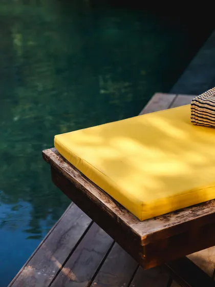 A simple, abstract shot of the yellow lounger cushion next to the deep green water of the pool.