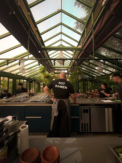 This is the view from the pass, my favorite spot in the house. It captures the essence of what we do: a chef, ready to perform, looking out at the intimate, sunlit stage of our glasshouse before the guests arrive.