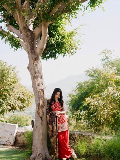 A full-length shot of the red kurta set against a tree, with a beautiful mountain view in the background.