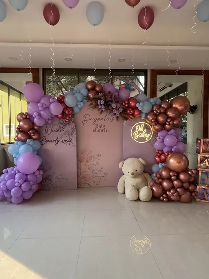 A "We can Bearly wait" baby shower setup in shades of lavender, blue, and rose gold, featuring a custom backdrop, neon sign, and teddy bear props.