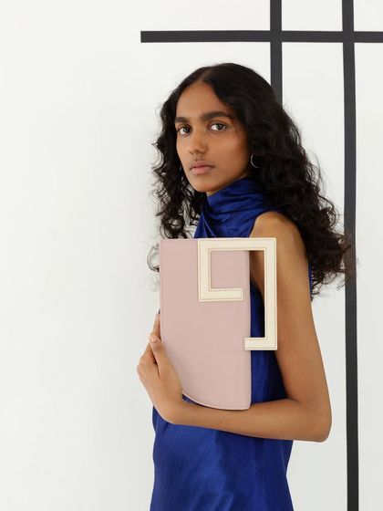 A portrait of a model holding a pink and white handbag. The composition and the model's direct gaze create a strong and engaging product-focused image.