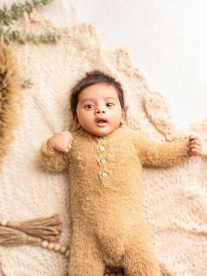 The most adorable little teddy bear! This newborn is dressed in a fuzzy, soft romper, looking so cozy and cute on a knitted blanket.