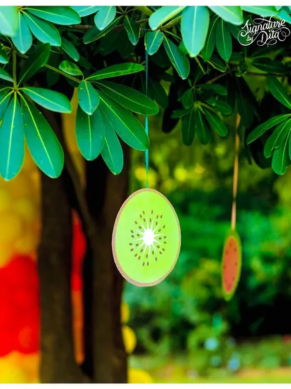 Hanging fruit slice decorations add a touch of whimsy to the trees around the party area. These small details help to extend the theme throughout the entire space.