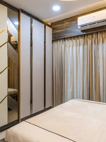 A bedroom in Mahad with a stylish wardrobe featuring white panels with gold chevron inlay and mirrored sections. This custom piece adds a touch of art deco glamour to the space.