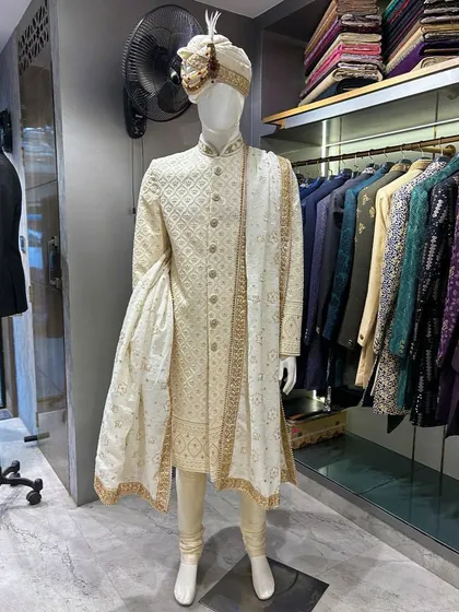 A classic groom's look never goes out of style. This is a beautifully crafted off-white sherwani with subtle self-embroidery, paired with a matching pagri (turban) and stole. It’s a testament to timeless elegance for the main wedding ceremony.