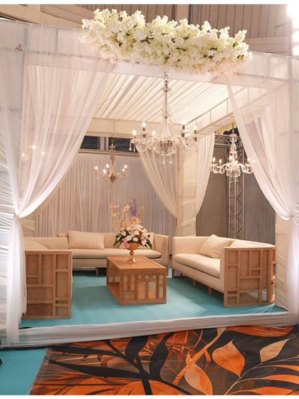 An elegant lounge area created within the grand reception hall. The modern wooden furniture, white drapes, and floral ceiling create a chic and comfortable space for guests to relax.