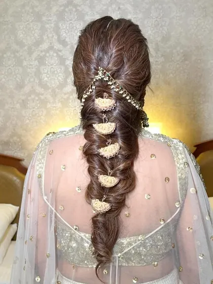 A close-up of the tassel details on a messy mehendi braid. The gold fan-shaped accessories add a unique, festive touch that elevates the entire hairstyle.
