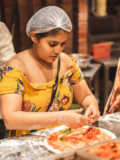 A participant concentrates on adding fresh basil to her pizza base. Our workshops guide you through every step of creating a classic Neapolitan pizza.