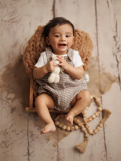 Look at that happy smile. This overhead shot captures the pure joy of a baby boy during his milestone session, using a simple setup with natural textures and a favorite toy.