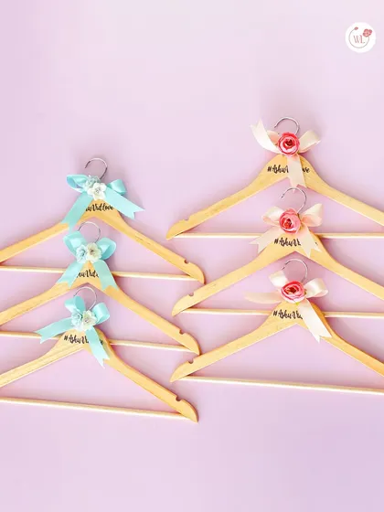 Custom hangers for the bride and groom's sides, differentiated by pink and blue ribbons.