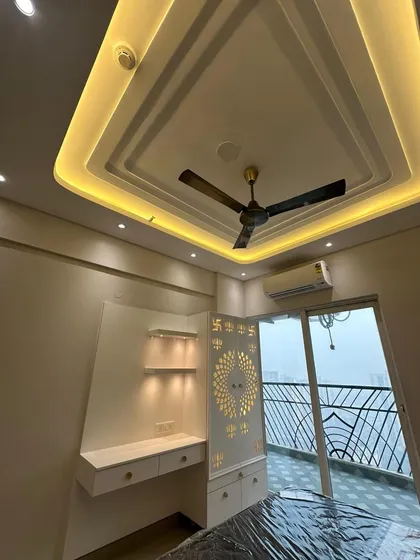 This bedroom corner was designed to be multi-functional. It includes a custom-built study desk with drawers and illuminated shelves, alongside a beautifully crafted pooja unit with a CNC-cut 'Swastik' panel. The multi-layered false ceiling with cove lighting adds a modern, ambient touch.