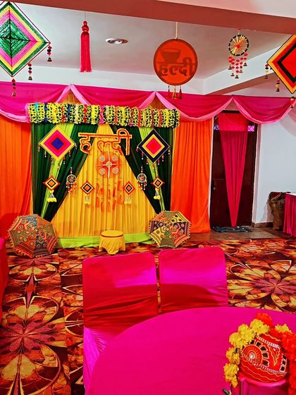 A Haldi ceremony setup inside a banquet hall, with a colourful backdrop, guest seating, and traditional decorative elements.