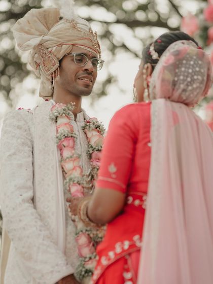 The groom's loving gaze as his bride approaches him for the varmala ceremony. This over-the-shoulder perspective makes the viewer feel present in this intimate and significant moment.
