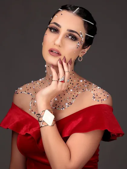 A glamorous editorial portrait with a model in a red dress, adorned with glitter and pearls on her skin for a high-fashion, artistic effect.