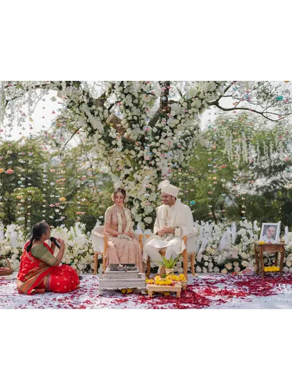 A female priest officiates the wedding, adding a modern and deeply personal touch to the traditional ceremony. The couple sits amidst a beautiful floral setup, fully present in the moment as they are united in marriage.