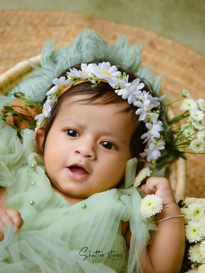 A lovely portrait of a baby girl in a green dress, nestled in a basket with white flowers.
