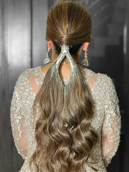 A unique and modern ponytail hairstyle, perfect for a cocktail or reception party. The hair is wrapped with a silver accessory for a chic finish.