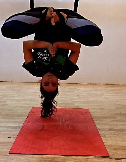 A student hangs in an inverted Baddha Konasana (Bound Angle Pose) within the aerial silk. This pose is excellent for spinal decompression and brings a calming effect to the mind.