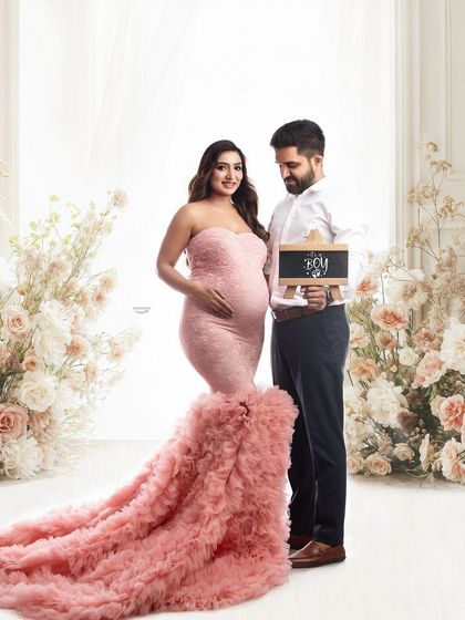 A lovely gender reveal photo. The couple stands amidst a beautiful floral setup as they announce 'It's a boy' with a small chalkboard sign, adding a personal touch to the session.