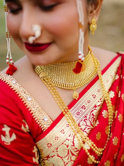 A close-up detail shot of the bride's stunning red saree with anchor motifs, her gold jewellery, and traditional 'mundavalya'.