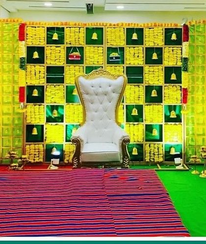 A classic Seemantham stage with a green and yellow checkerboard backdrop. The setup includes an ornate white throne and is ready for the ceremony with a traditional woven mat.
