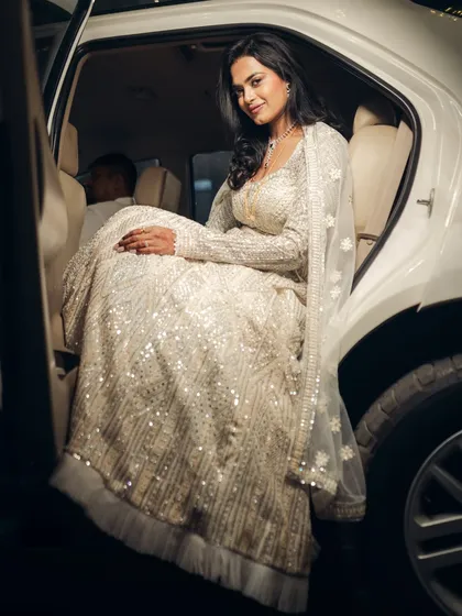 A glamorous shot of the bride in her sparkling white lehenga, stepping out of the car. This image has a modern, celebrity-like feel, perfect for a stylish reception entrance.