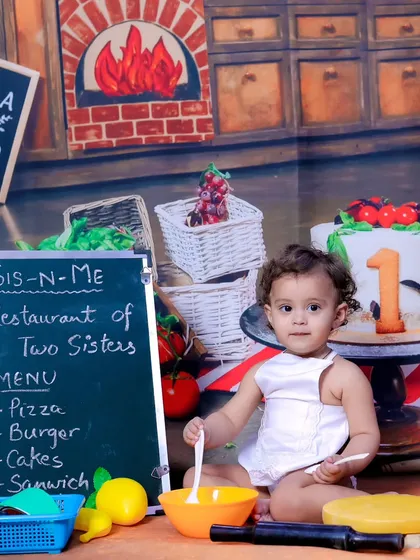 A little chef in her own pizzeria. The chalkboard menu and kitchen backdrop create an immersive and fun setting.