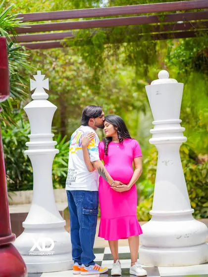 A sweet moment with the partner kissing the mother-to-be's forehead on the giant chessboard set.